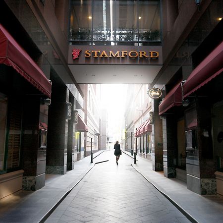 Hotel Stamford Plaza Melbourne City Exterior foto The photo depicts a narrow alley or passageway, possibly in an urban setting. On one side, there are storefronts with canopies, and on the opposite side, there is a prominent sign reading "STAMFORD." The pathway is lined with buildings, creating a se