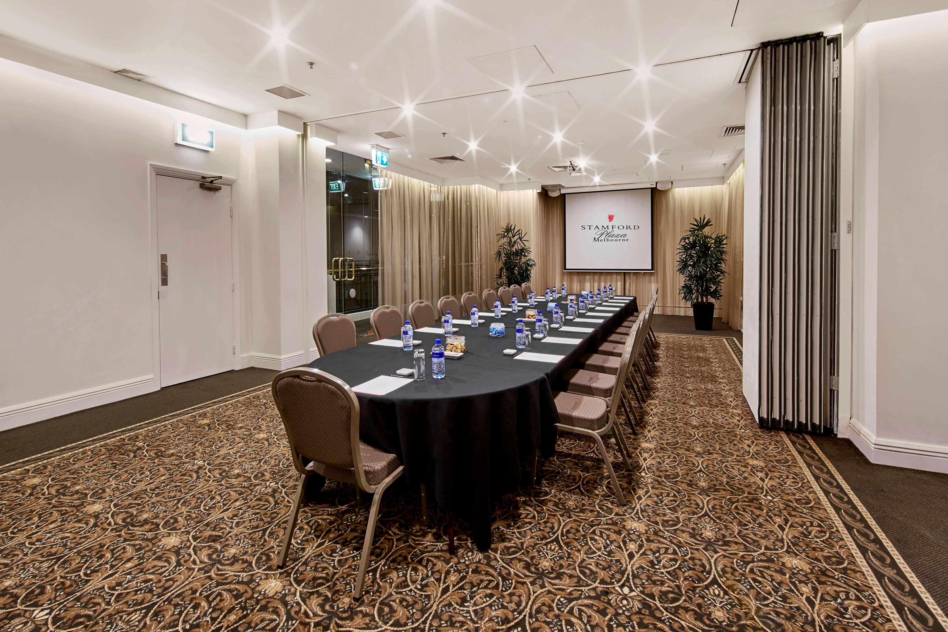Hotel Stamford Plaza Melbourne City Exterior foto The photo shows a meeting room set up for a conference or presentation. There is a long, rectangular table covered with a black tablecloth, surrounded by chairs. Each seat has a water bottle placed in front of it. At the front of the room, there is a