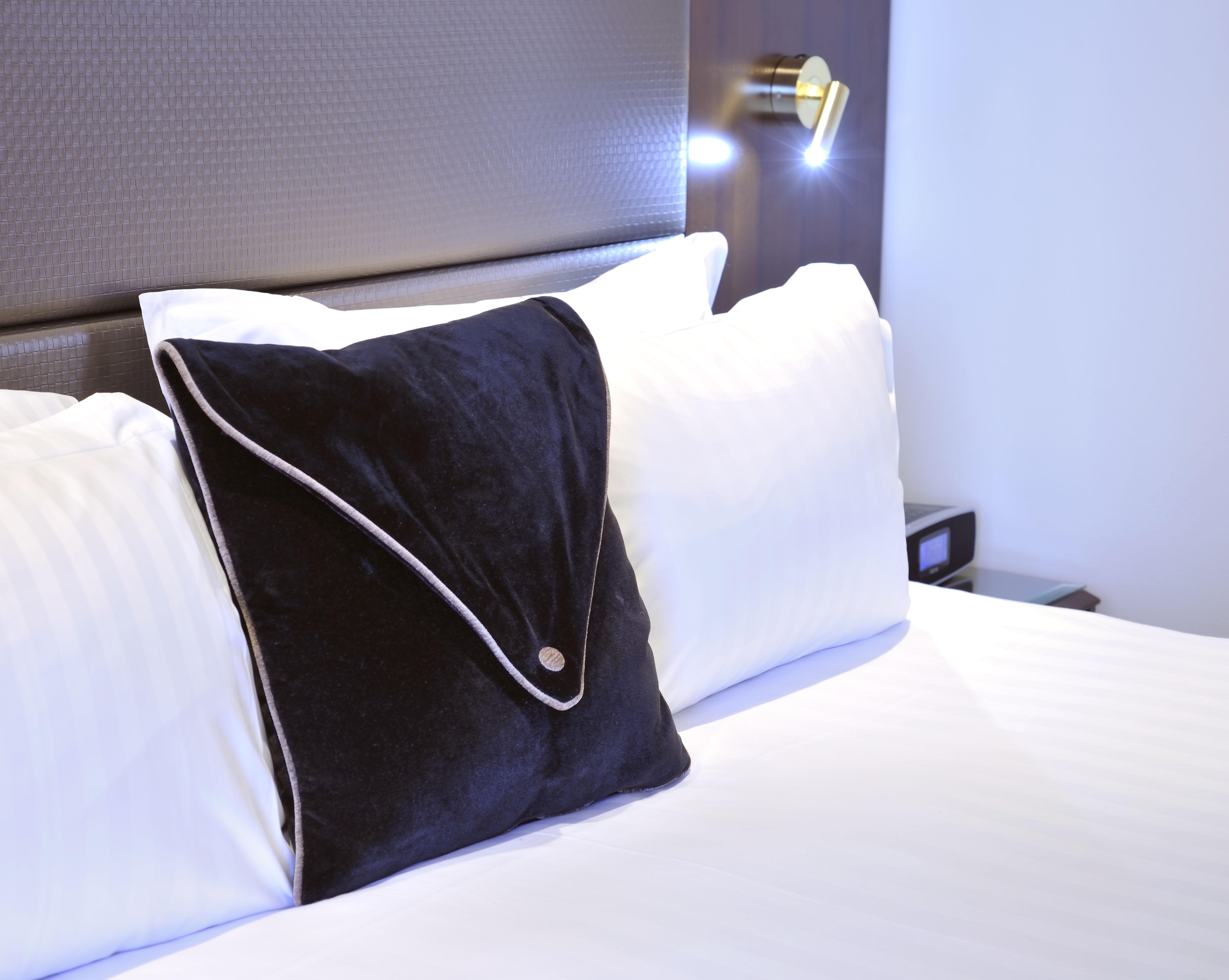 Hotel Stamford Plaza Melbourne City Exterior foto The photo shows a neatly arranged bed with white linens. There are several pillows, with one black pillow featuring a distinctive design on top of the white pillows. The headboard of the bed is visible, along with a stylish wall-mounted light fixture