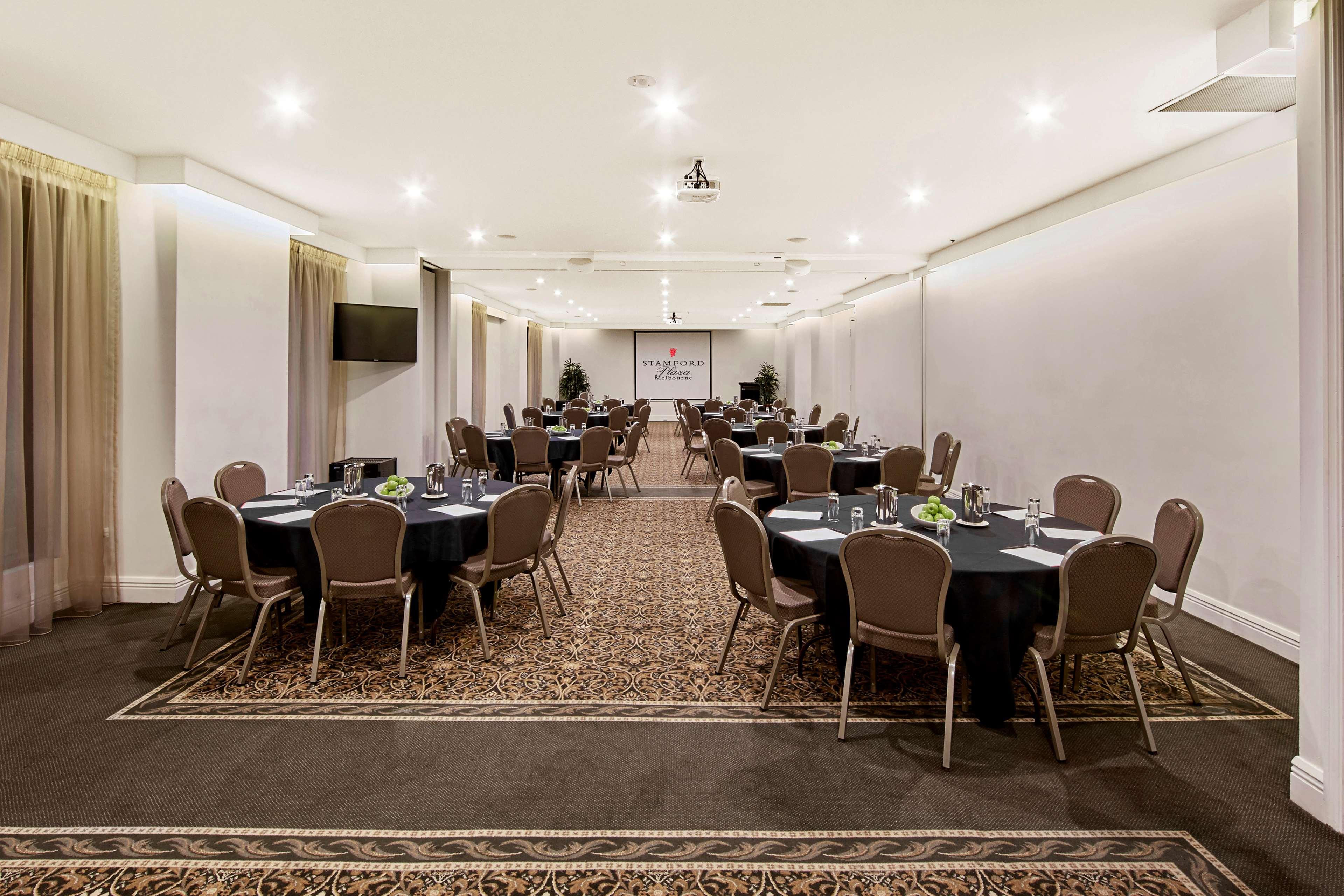 Hotel Stamford Plaza Melbourne City Exterior foto The photo shows an event space or banquet hall set up for a gathering. The room features several round tables covered with black tablecloths, each adorned with small centerpieces. Chairs are arranged around each table. The lighting is bright and mode
