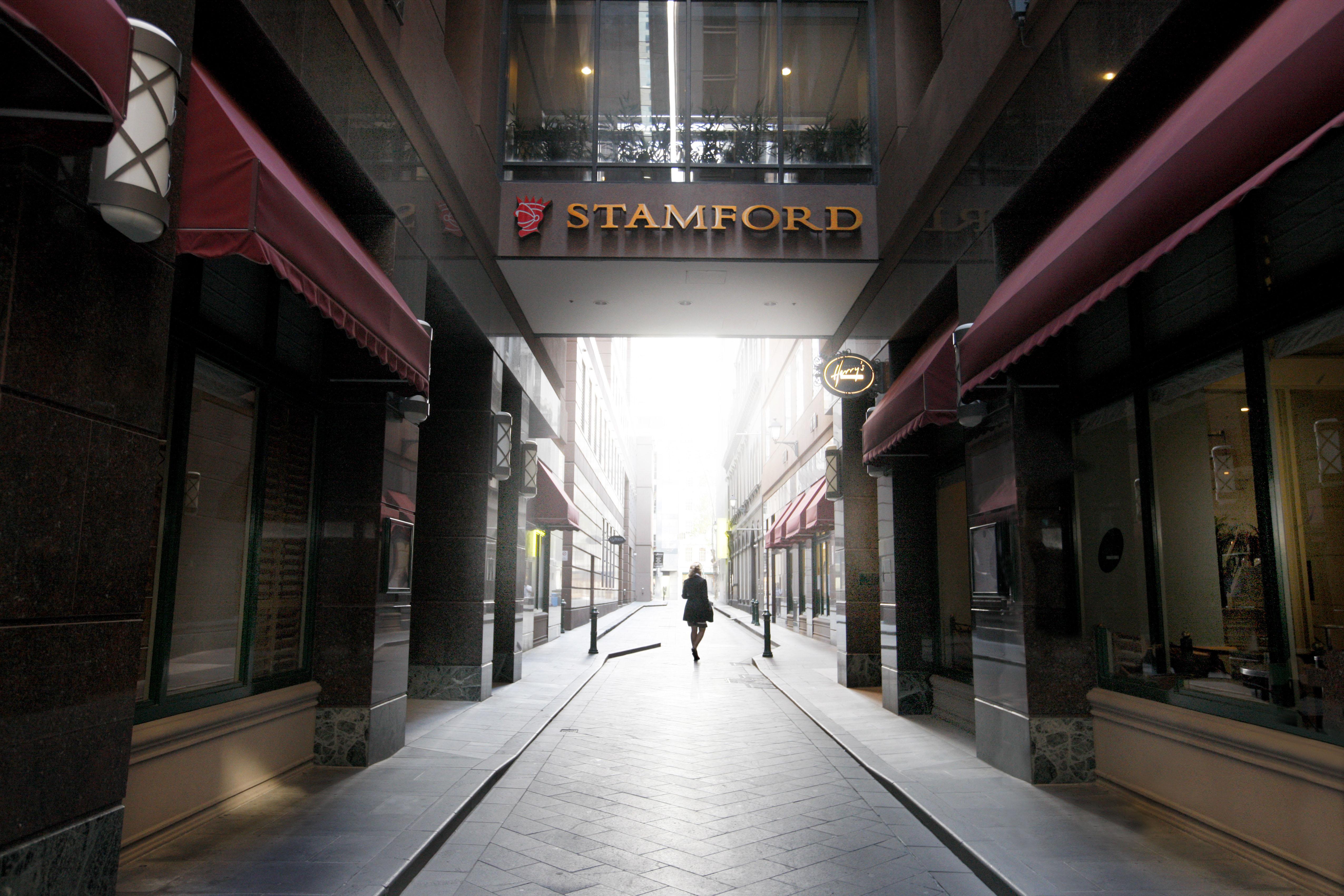 Hotel Stamford Plaza Melbourne City Exterior foto The photo depicts a narrow alley or passageway, possibly in an urban setting. On one side, there are storefronts with canopies, and on the opposite side, there is a prominent sign reading "STAMFORD." The pathway is lined with buildings, creating a se