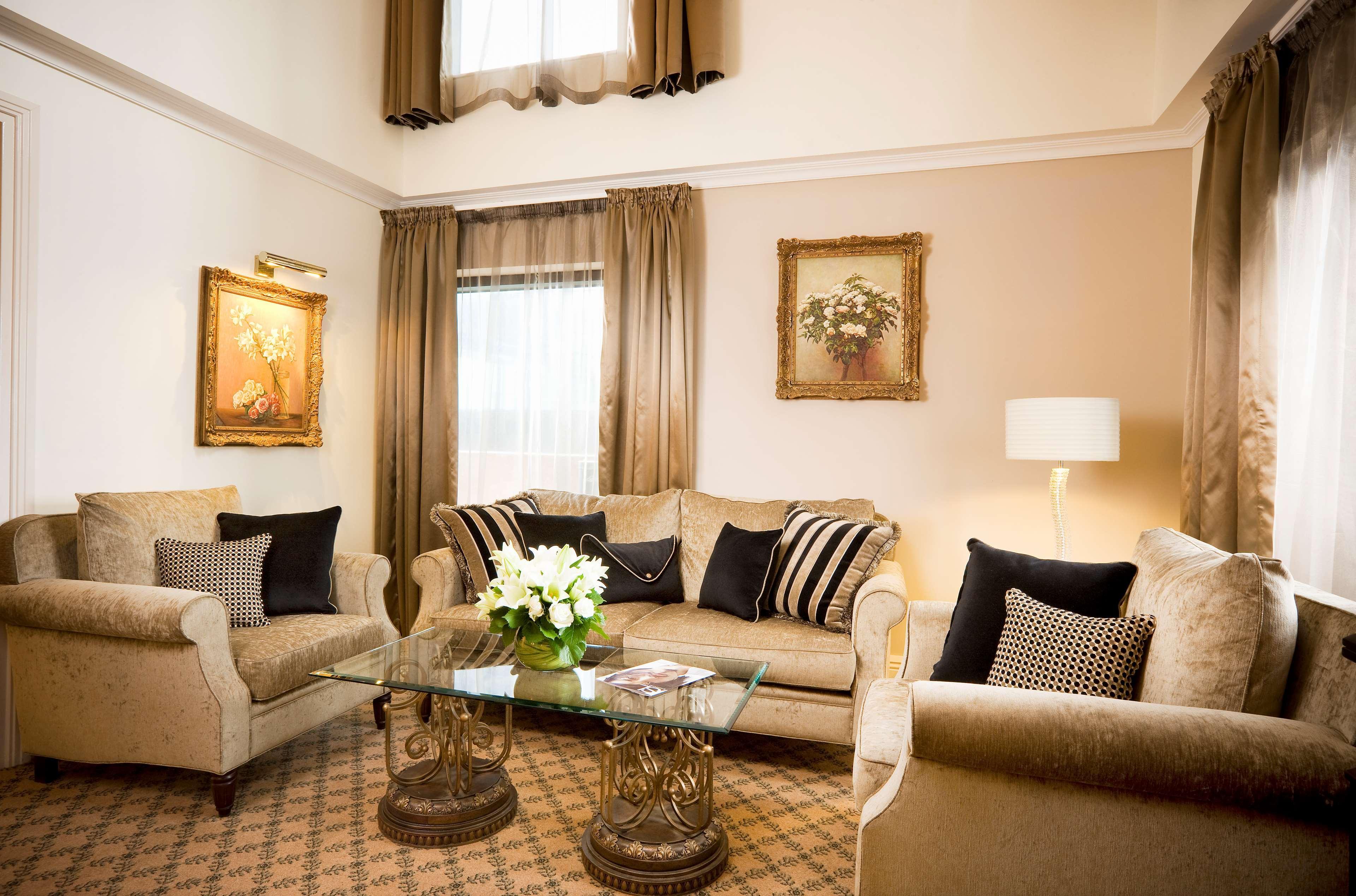 Hotel Stamford Plaza Melbourne City Zimmer foto The photo depicts a stylish living room with a warm and inviting aesthetic. It features a set of comfortable beige sofas adorned with decorative pillows in black and patterned designs. There is a glass coffee table at the center, supported by elegant
