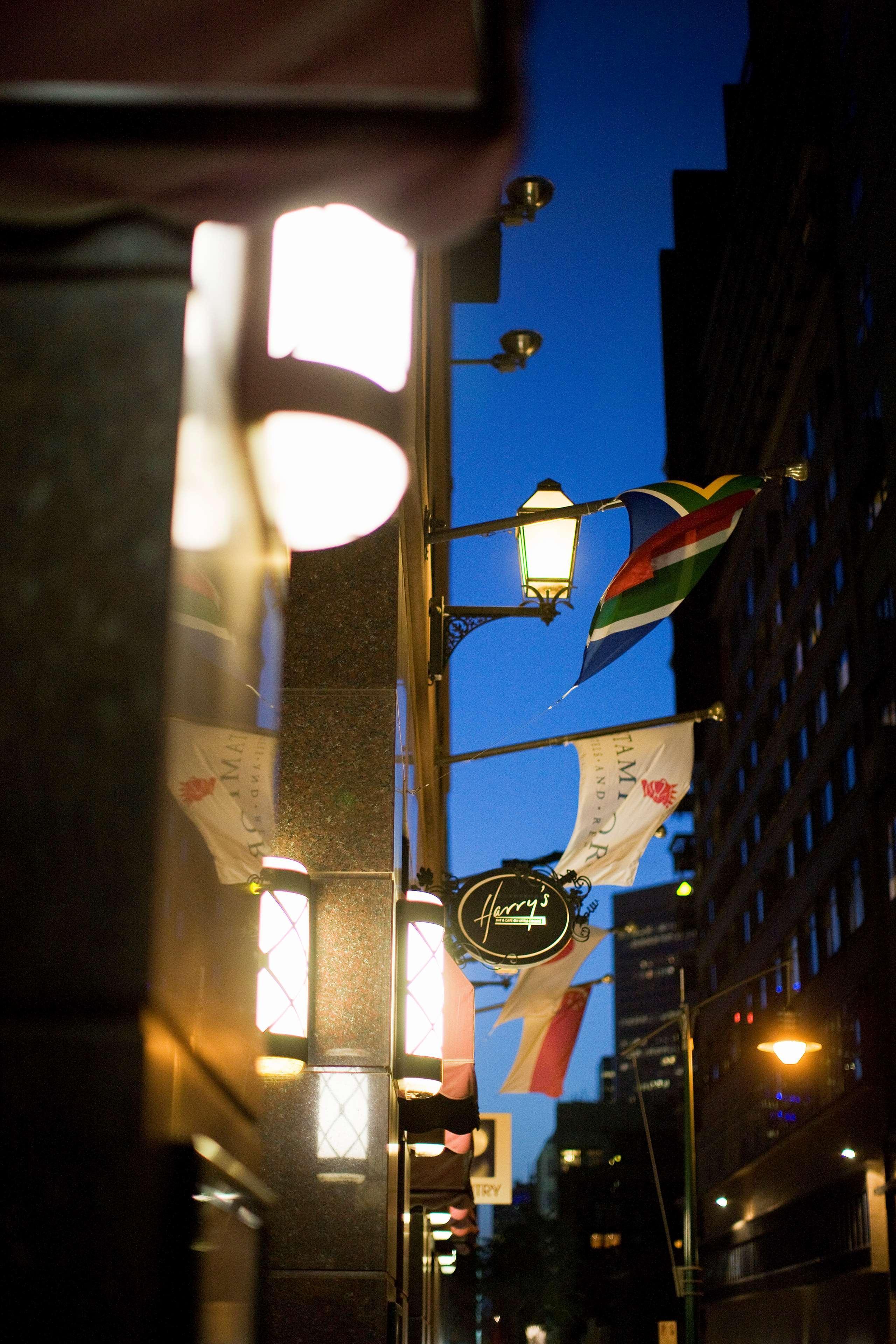 Hotel Stamford Plaza Melbourne City Exterior foto The photo features a street view of a building at dusk. Prominently displayed are several flags, including a South African flag, which are fluttering in the wind. There is a sign that reads "Harry's," likely indicating the name of a business or estab