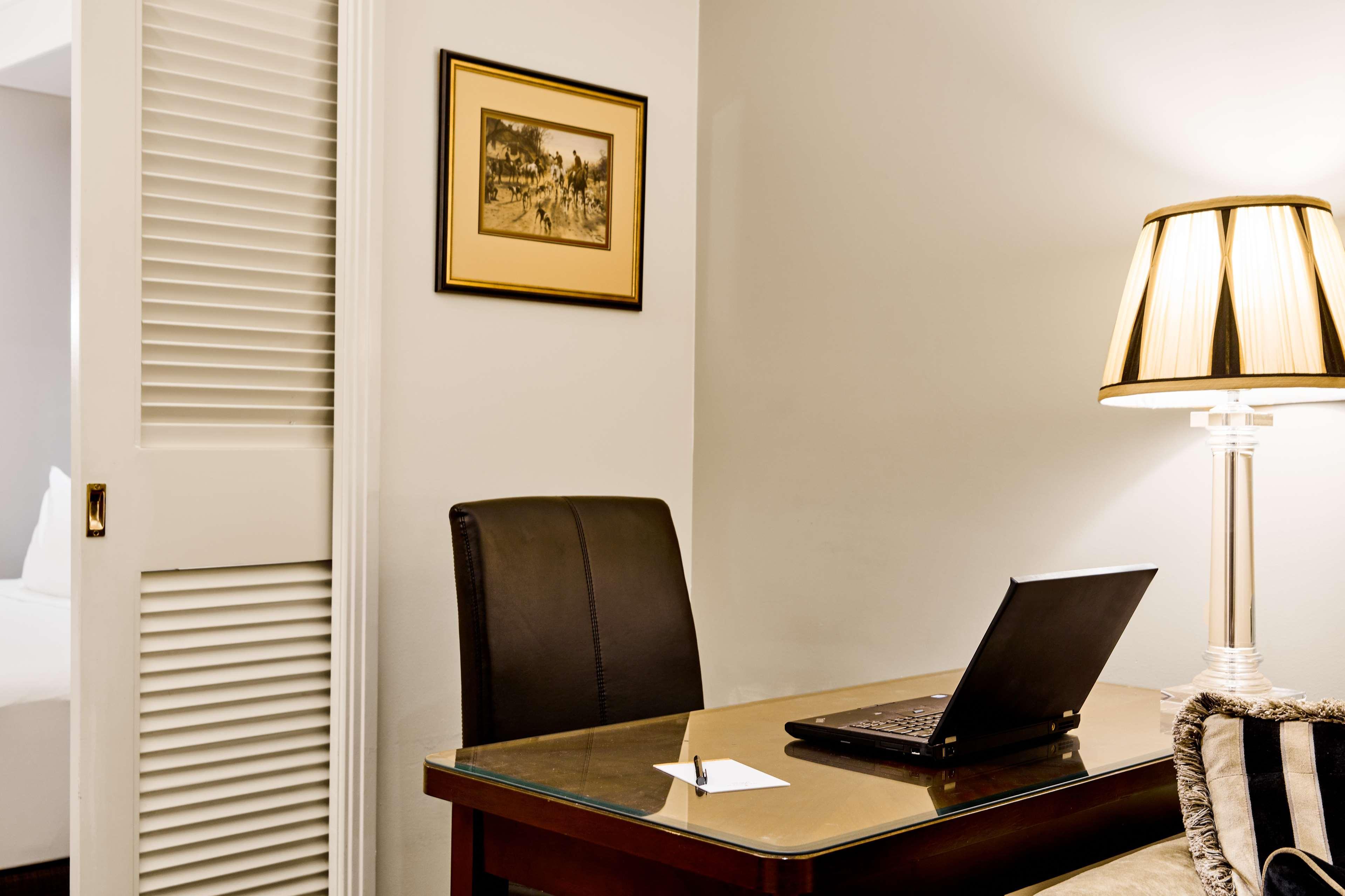 Hotel Stamford Plaza Melbourne City Exterior foto The photo shows a small office or workspace. There is a desk with a glass surface, and on it sits a laptop computer. A piece of paper or notecard is also placed on the desk. Behind the desk is a black office chair. A wall lamp with a striped shade is