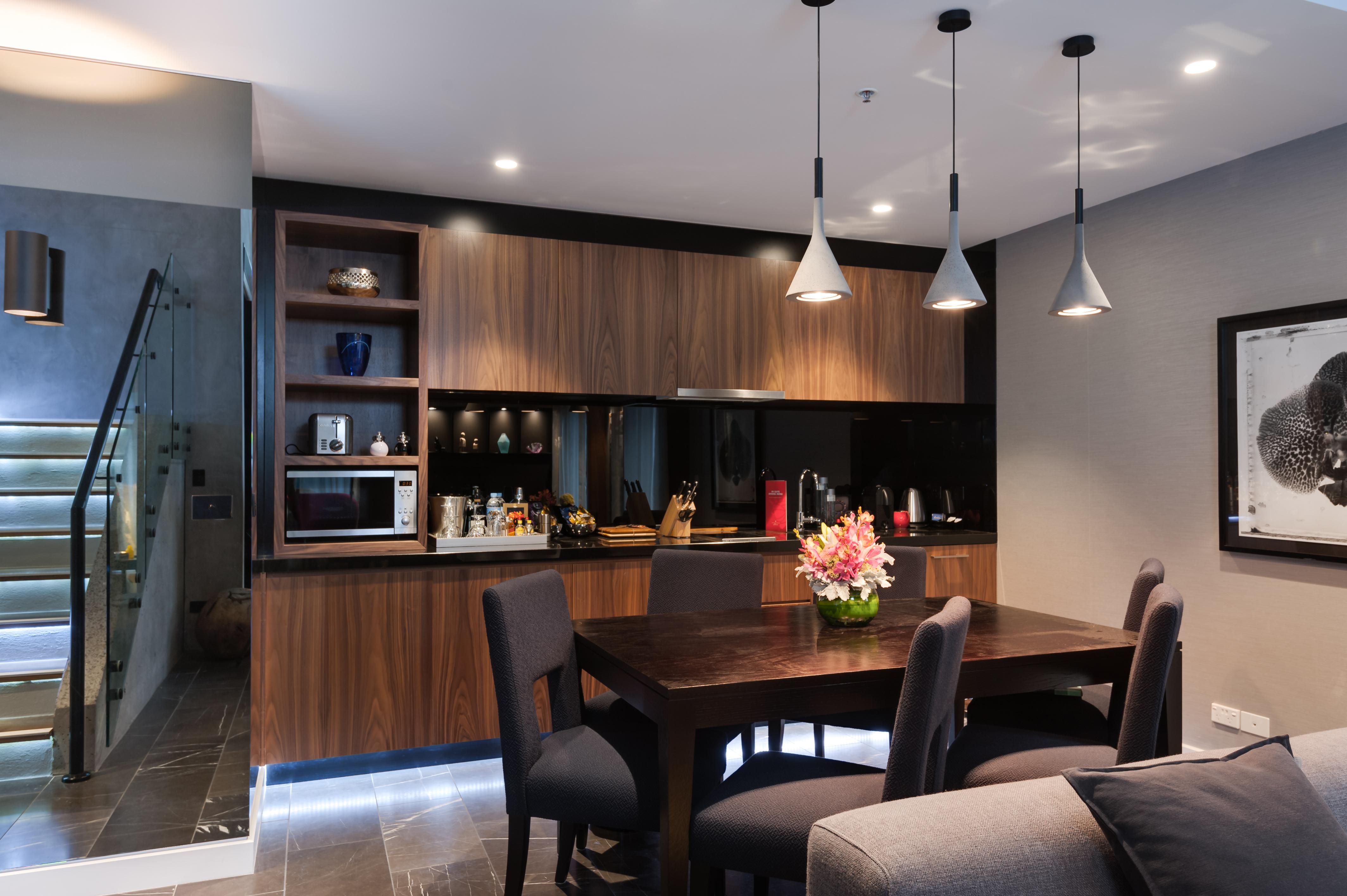 Hotel Stamford Plaza Melbourne City Exterior foto The image shows a modern kitchen and dining area. The kitchen features dark wooden cabinetry with black accents, a microwave, and various kitchen items arranged on the shelves. There is a dining table made of dark wood, surrounded by several chairs. 