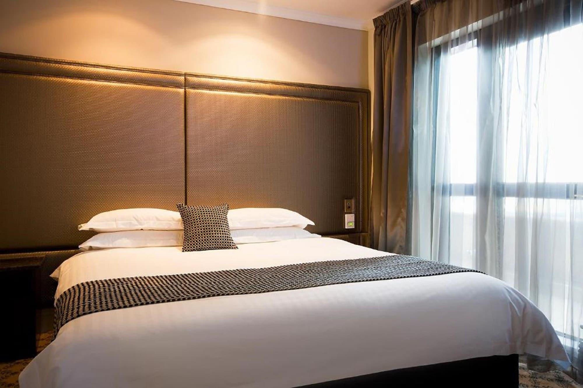 Hotel Stamford Plaza Melbourne City Exterior foto The photo shows a modern bedroom featuring a large bed with a neatly arranged white comforter and decorative pillows. The headboard is upholstered in a dark material, and there is soft lighting above it. On one side of the bed, there’s a small decora