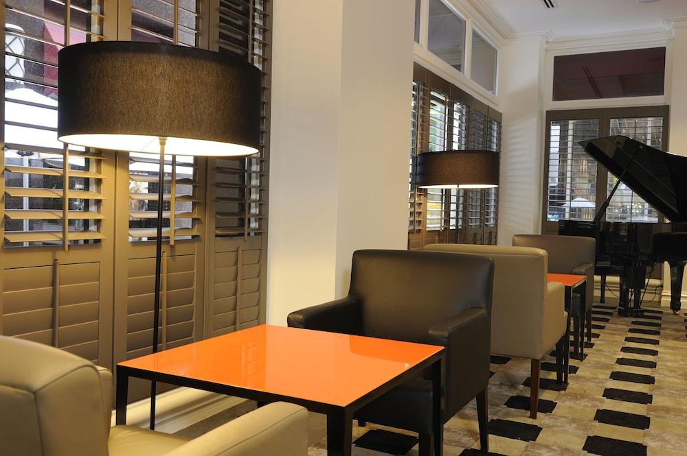 Hotel Stamford Plaza Melbourne City Exterior foto The photo shows a cozy interior space, likely a lounge or café. It features a modern design with a mix of seating options, including black and light-colored chairs surrounding small tables. One table has a bright orange top, creating a striking visua