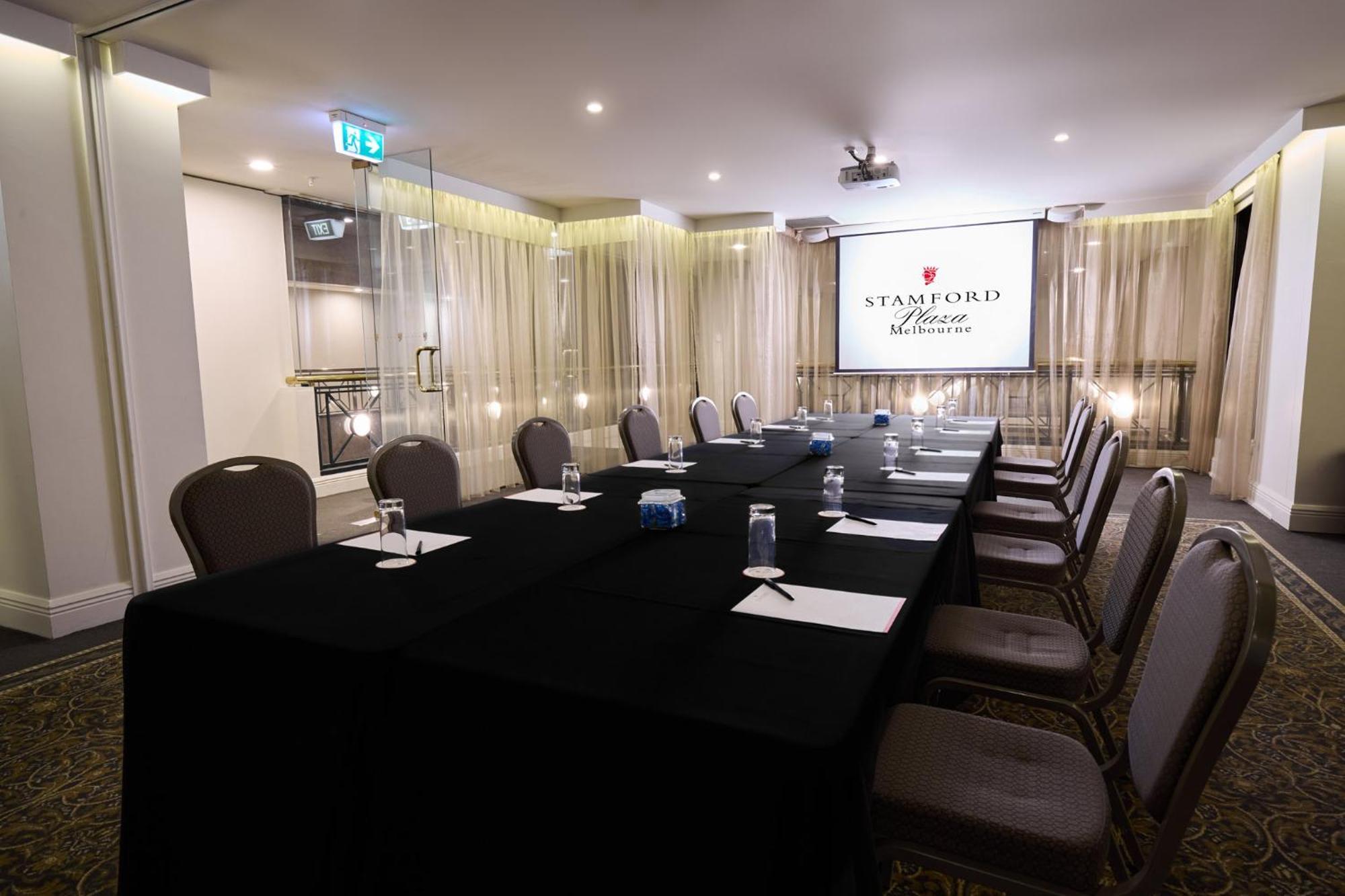 Hotel Stamford Plaza Melbourne City Exterior foto The photo shows a well-appointed conference room designed for meetings or presentations. There is a long rectangular table covered with a black tablecloth, surrounded by upholstered chairs. On the table, there are several folded pieces of paper and g