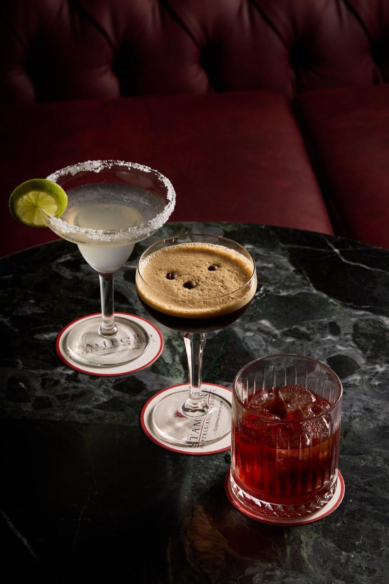 Hotel Stamford Plaza Melbourne City Exterior foto The photo displays three different cocktails arranged on a dark marble table. 

1. On the left, there is a margarita glass filled with a clear drink, garnished with a lime slice and featuring a salted rim.
2. In the center, a coupe glass holds a dark
