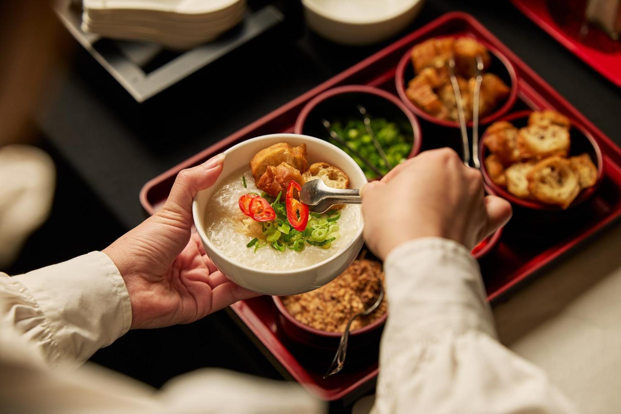 Hotel Stamford Plaza Melbourne City Exterior foto The photo shows a person serving food from a tray filled with various dishes. In one hand, they are holding a bowl filled with a creamy, likely rice-based dish topped with slices of chili and possibly fried tofu or other toppings. Surrounding the bow