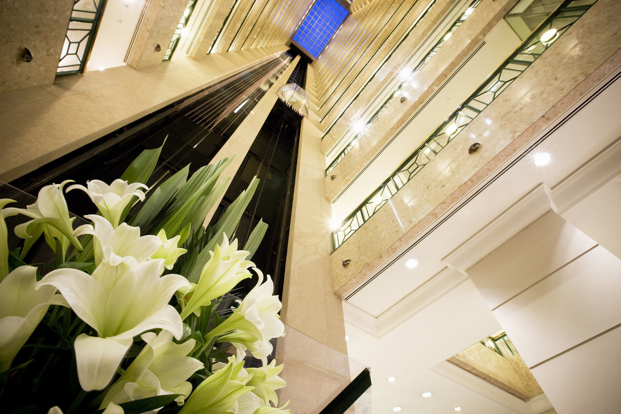 Hotel Stamford Plaza Melbourne City Interior foto The photo shows a modern indoor space, likely a lobby or atrium of a building. The view is looking upwards, capturing a sleek design with multiple levels. There are several elevators in the center, running vertically. The walls are lined with glass a